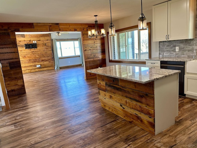 kitchen featuring light stone countertops, dark hardwood / wood-style flooring, wooden walls, white cabinets, and a kitchen island