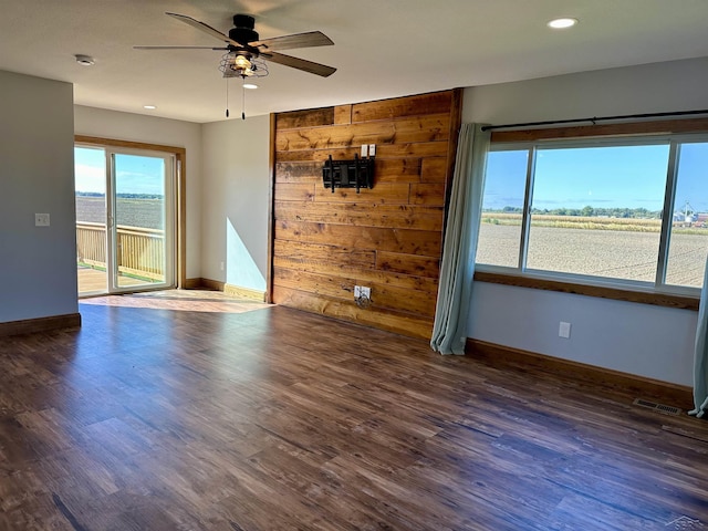 empty room with ceiling fan, dark wood-type flooring, and wood walls