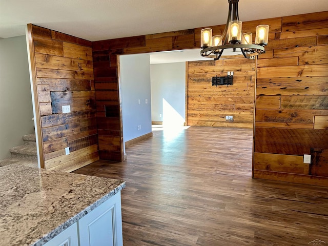 dining room featuring wooden walls, dark wood-type flooring, and an inviting chandelier