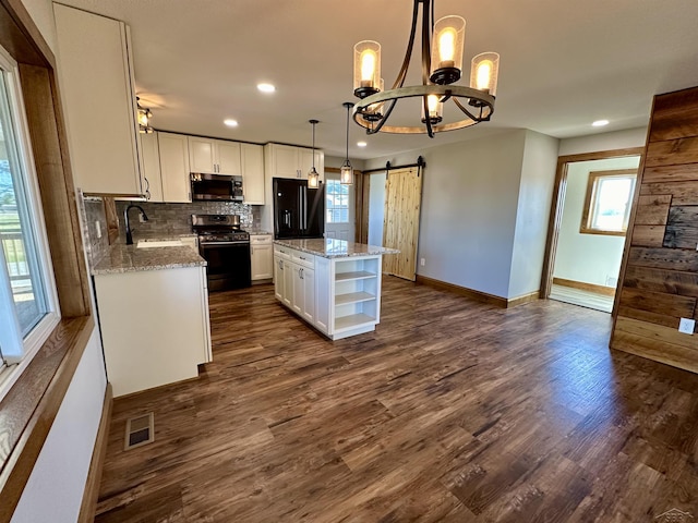 kitchen with a barn door, a center island, white cabinetry, and black appliances