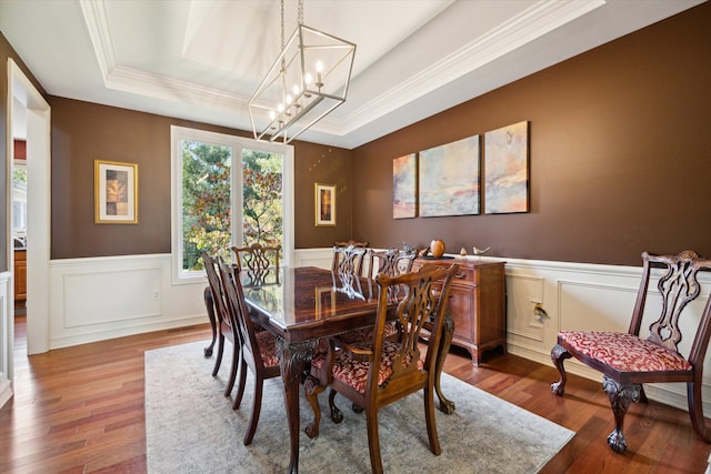 dining area featuring a tray ceiling, an inviting chandelier, ornamental molding, and hardwood / wood-style flooring