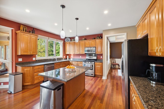 kitchen with sink, hanging light fixtures, stainless steel appliances, hardwood / wood-style floors, and a kitchen island