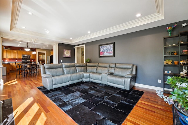 living room featuring a raised ceiling, wood-type flooring, and ornamental molding