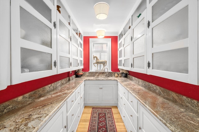 bar featuring stone counters, light hardwood / wood-style floors, white cabinetry, and sink