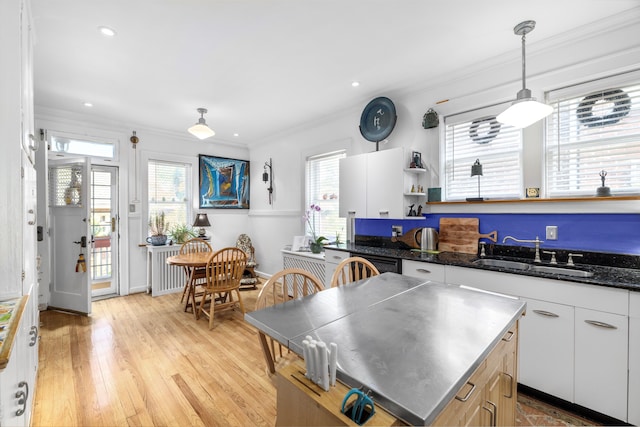 kitchen with white cabinets, light wood-type flooring, sink, and hanging light fixtures