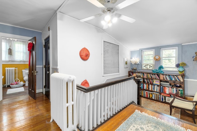 corridor featuring wood-type flooring, radiator heating unit, crown molding, and vaulted ceiling