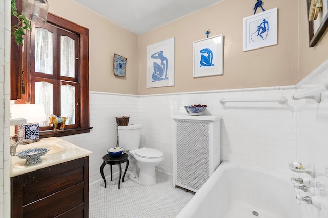 bathroom with tile patterned floors, toilet, a bathtub, vanity, and tile walls