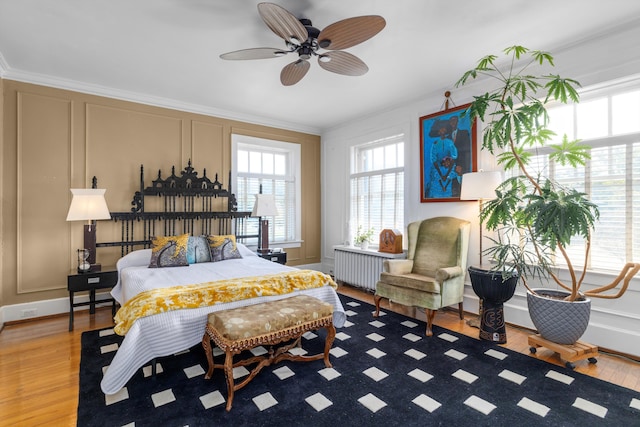 bedroom featuring ceiling fan, light wood-type flooring, radiator heating unit, and ornamental molding