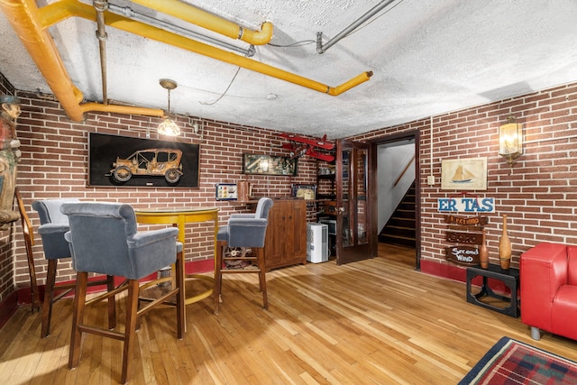 bar featuring a textured ceiling, hardwood / wood-style flooring, and brick wall