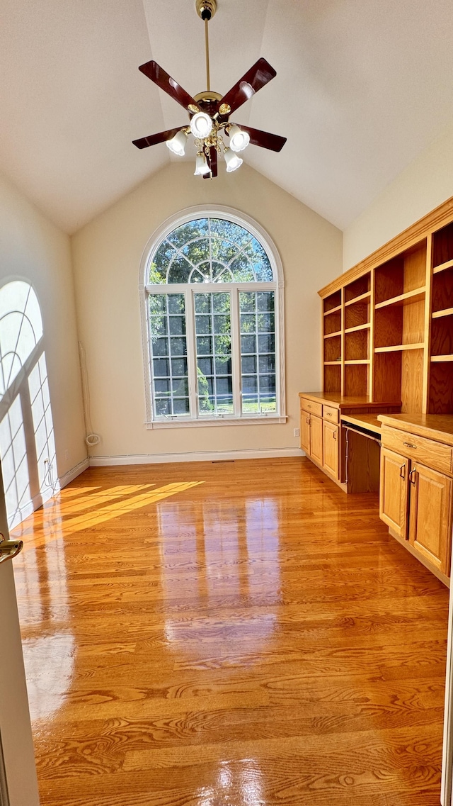 interior space featuring ceiling fan, built in desk, vaulted ceiling, and light hardwood / wood-style floors