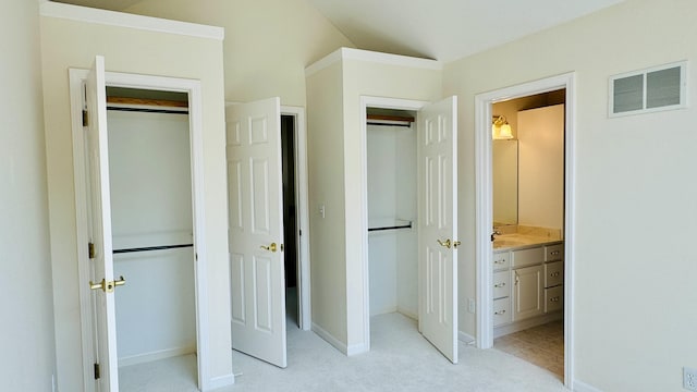 unfurnished bedroom with ensuite bathroom, a closet, light colored carpet, and lofted ceiling