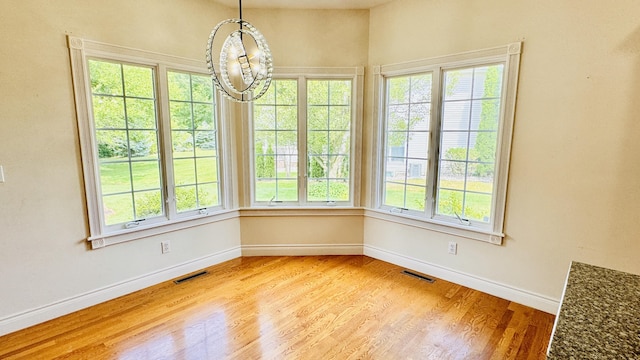 unfurnished dining area featuring plenty of natural light, light wood-type flooring, and an inviting chandelier