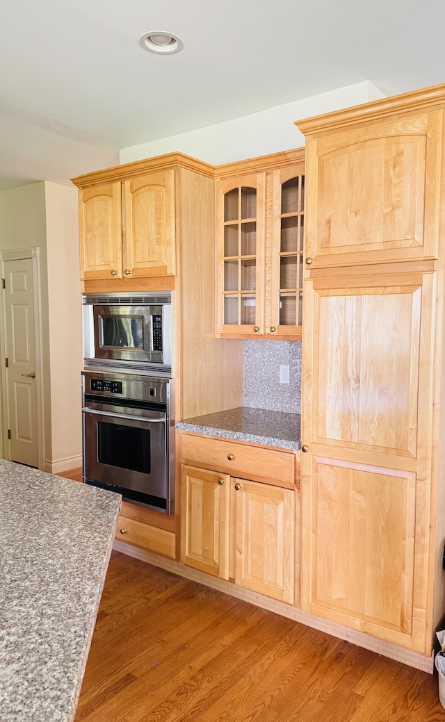 kitchen with decorative backsplash, light brown cabinets, stainless steel appliances, and light hardwood / wood-style floors