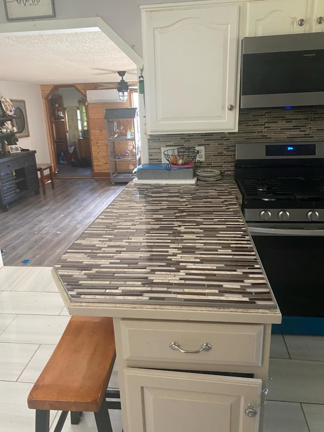 kitchen featuring tasteful backsplash, black gas range oven, a textured ceiling, wood-type flooring, and white cabinets