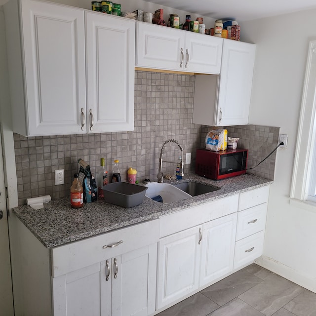 kitchen with white cabinetry, sink, backsplash, and light stone countertops