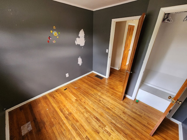 unfurnished bedroom with light wood-type flooring, ornamental molding, and a closet