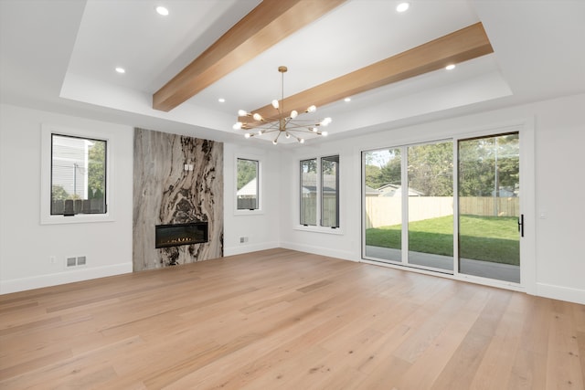 unfurnished living room with beamed ceiling, a chandelier, a high end fireplace, and light hardwood / wood-style flooring