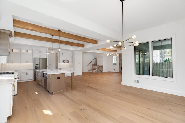 kitchen with pendant lighting, light hardwood / wood-style flooring, an island with sink, beamed ceiling, and white cabinetry