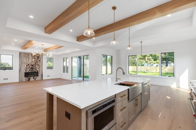 kitchen featuring a center island with sink, a high end fireplace, hanging light fixtures, and light hardwood / wood-style flooring