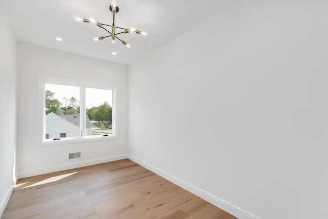 spare room featuring a notable chandelier and light wood-type flooring