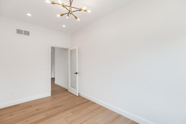 spare room with an inviting chandelier and light hardwood / wood-style flooring