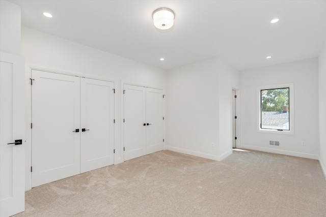 unfurnished bedroom with multiple closets and light carpet