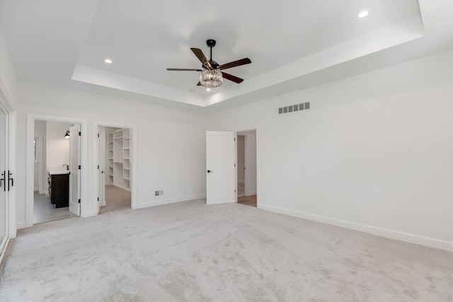 unfurnished bedroom featuring light carpet, a walk in closet, ceiling fan, a tray ceiling, and a closet