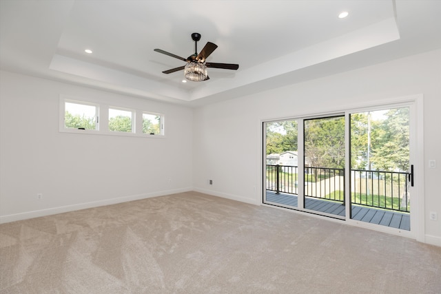 unfurnished room featuring light carpet, a tray ceiling, and ceiling fan