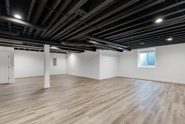 basement featuring electric panel and light hardwood / wood-style flooring