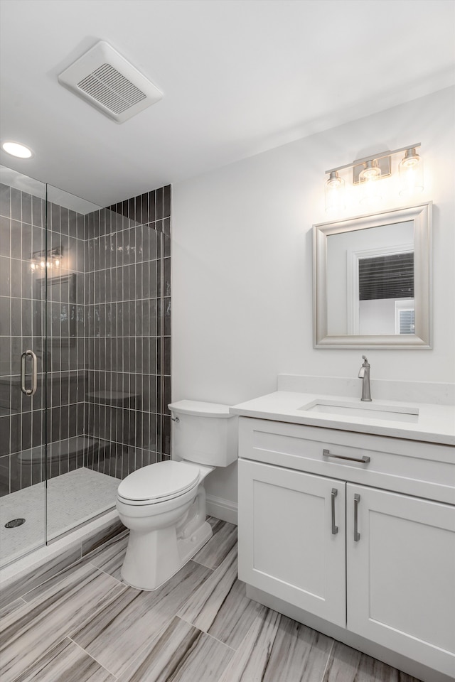 bathroom featuring a shower with door, vanity, and toilet