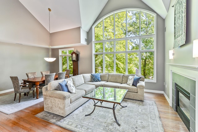 living room with light hardwood / wood-style floors, high vaulted ceiling, and a tiled fireplace