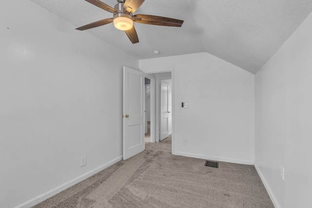 interior space with a textured ceiling, light colored carpet, vaulted ceiling, and ceiling fan