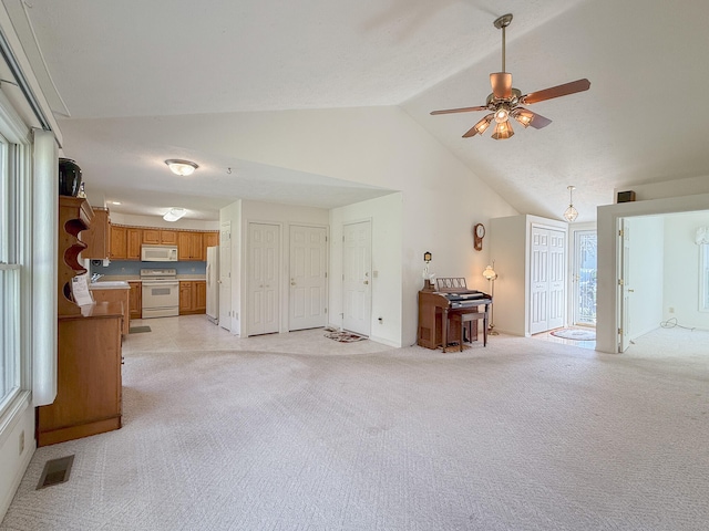 unfurnished living room with ceiling fan, a healthy amount of sunlight, light colored carpet, and vaulted ceiling