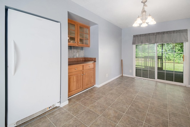 interior space with pendant lighting, white refrigerator, an inviting chandelier, and light tile patterned flooring