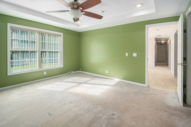 carpeted spare room with a raised ceiling and ceiling fan