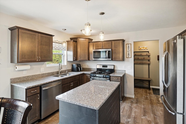 kitchen featuring a center island, decorative light fixtures, stainless steel appliances, sink, and light stone counters