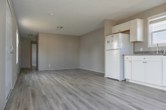 kitchen featuring light stone countertops, white cabinetry, sink, white refrigerator, and light hardwood / wood-style floors