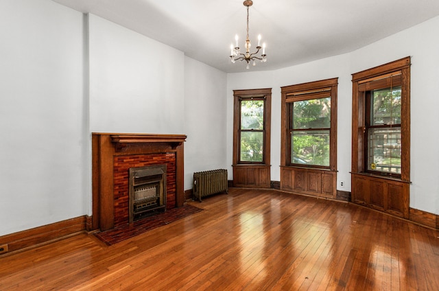 unfurnished living room featuring hardwood / wood-style floors, a brick fireplace, radiator, and an inviting chandelier