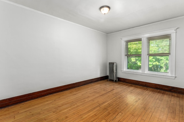 empty room with radiator heating unit, light wood-type flooring, and crown molding