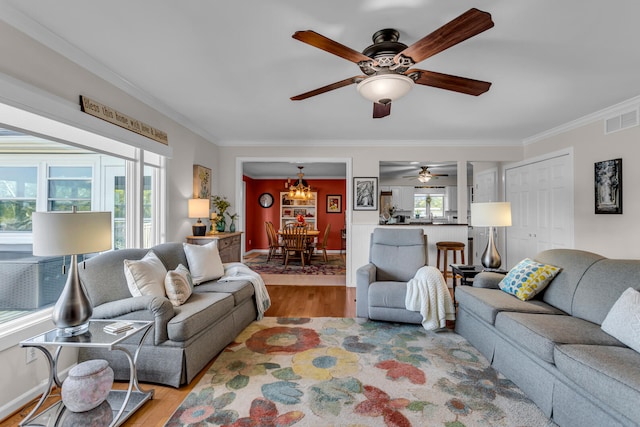 living room with ceiling fan with notable chandelier, light hardwood / wood-style floors, and crown molding