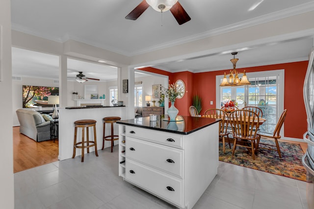 kitchen with white cabinets, a center island, ceiling fan with notable chandelier, and crown molding