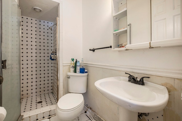 bathroom featuring tile patterned floors, sink, tiled shower, tile walls, and toilet