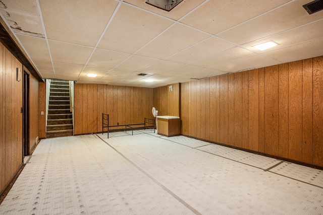 basement featuring a paneled ceiling and wooden walls