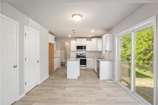 kitchen with sink, tasteful backsplash, decorative light fixtures, white cabinets, and appliances with stainless steel finishes