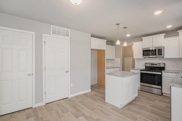 kitchen featuring light wood-type flooring, backsplash, stainless steel appliances, decorative light fixtures, and white cabinetry