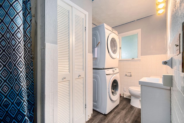 clothes washing area featuring tile walls, dark hardwood / wood-style floors, and stacked washer and clothes dryer