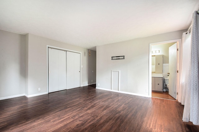 unfurnished bedroom featuring ensuite bathroom, a closet, and dark hardwood / wood-style floors