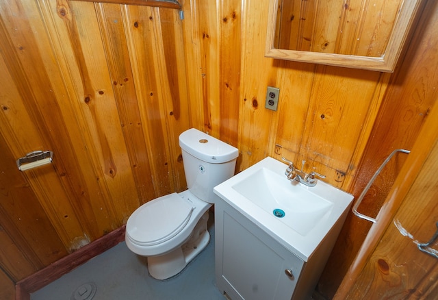 bathroom with vanity, toilet, and wood walls