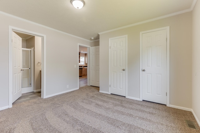 unfurnished bedroom with carpet flooring, ensuite bath, crown molding, and multiple closets