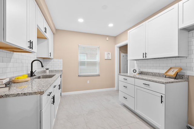 kitchen with white cabinets, decorative backsplash, light stone counters, and sink